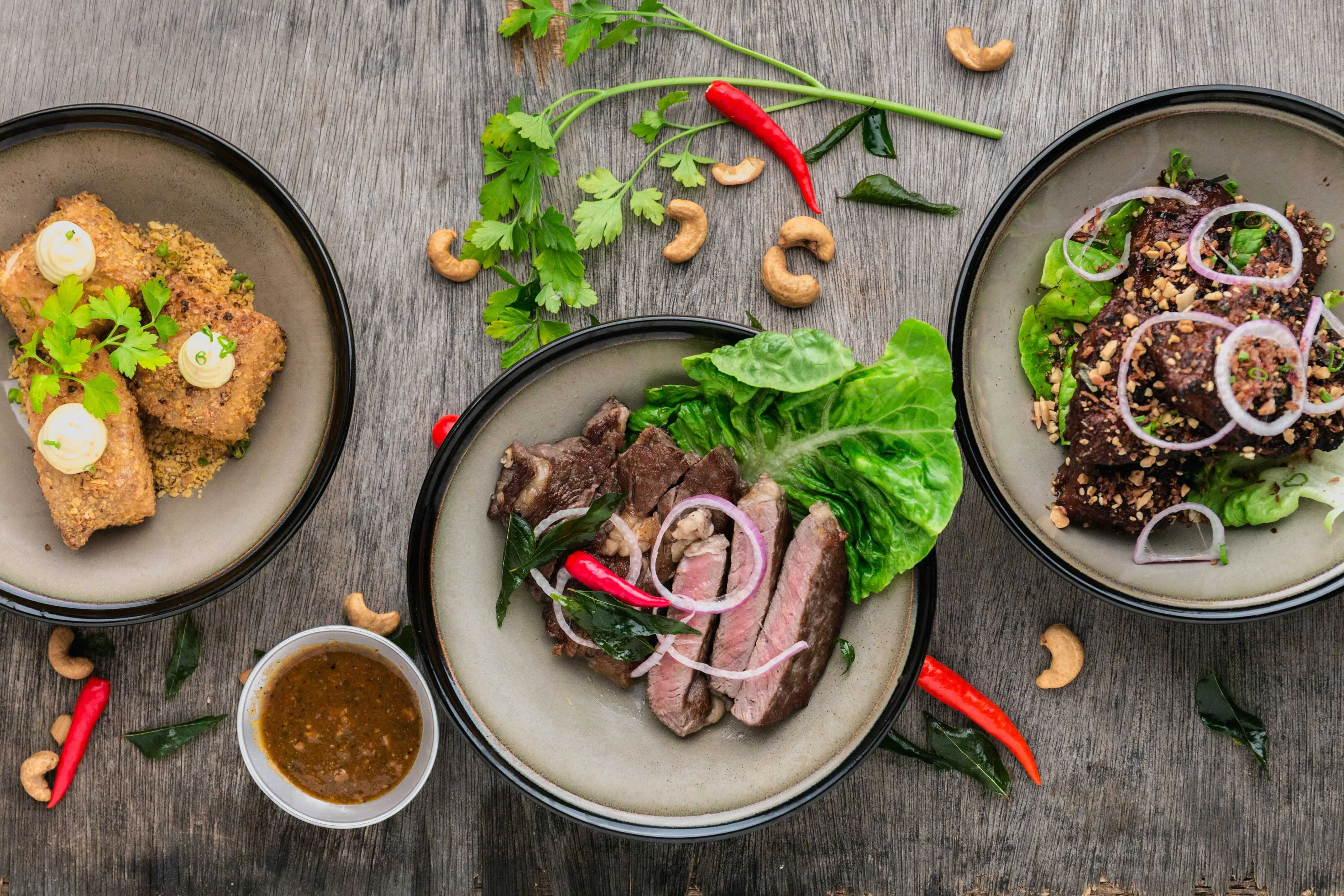 Image of 3 dishes of fishcakes, sliced beef salad and something brown. By Lily Banse.